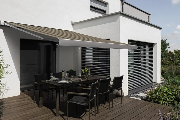 Modernes Wohnhaus mit ausgefahrener Markise und Raffstoren, davor eine sonnige Terrasse